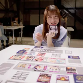 Kanna Hashimoto segura cartas diante de uma mesa de One Piece Card Game em cena promocional da Bandai